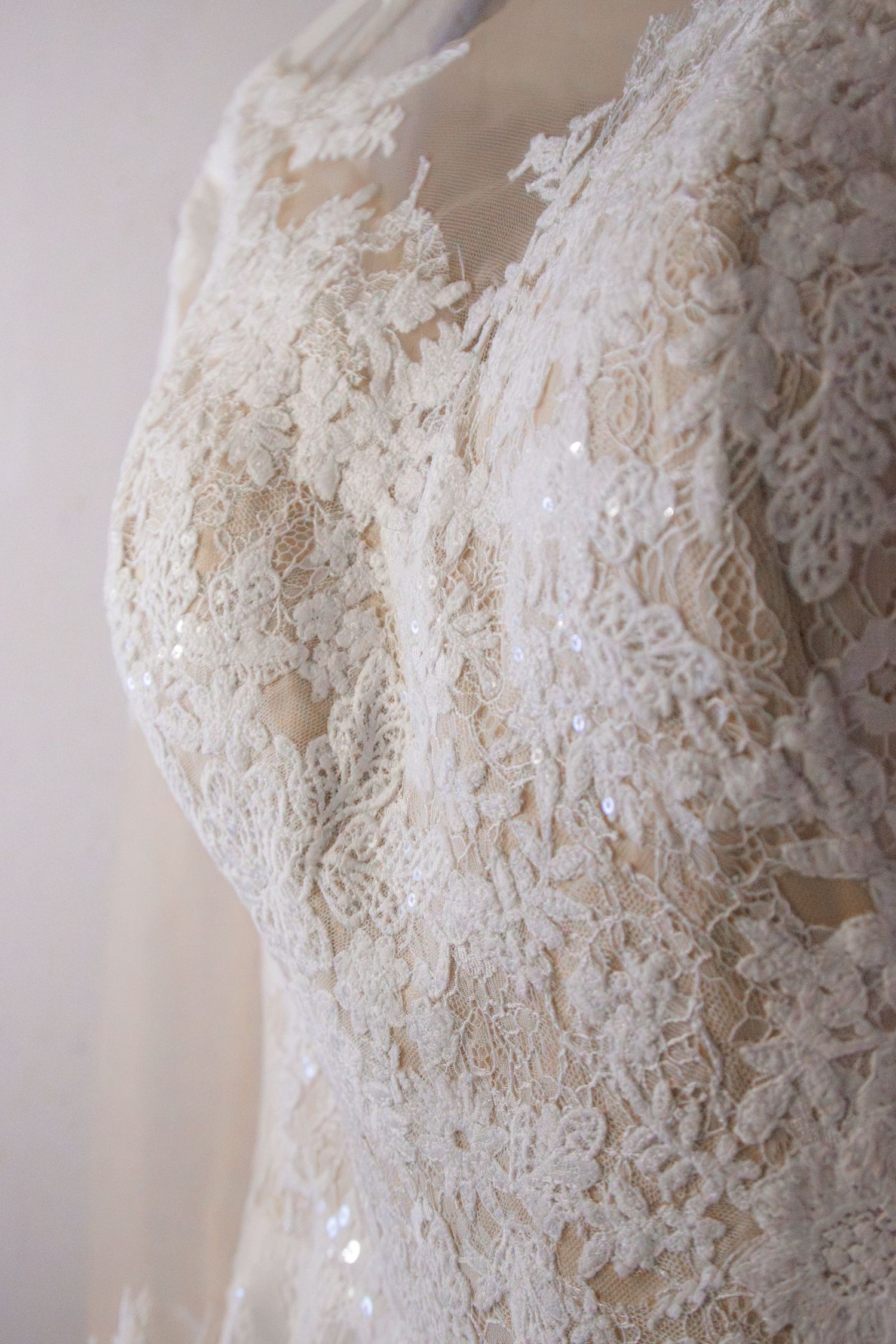 Close-up of an elegant white lace wedding dress with sequin details and V-neckline on a mannequin.