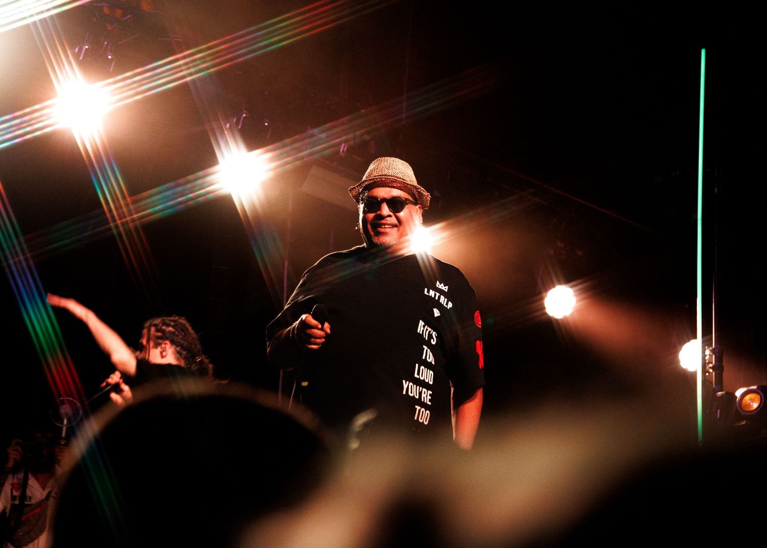 A series of dark concert photos with lens flares showing silhouettes of performers on stage under dramatic lighting.