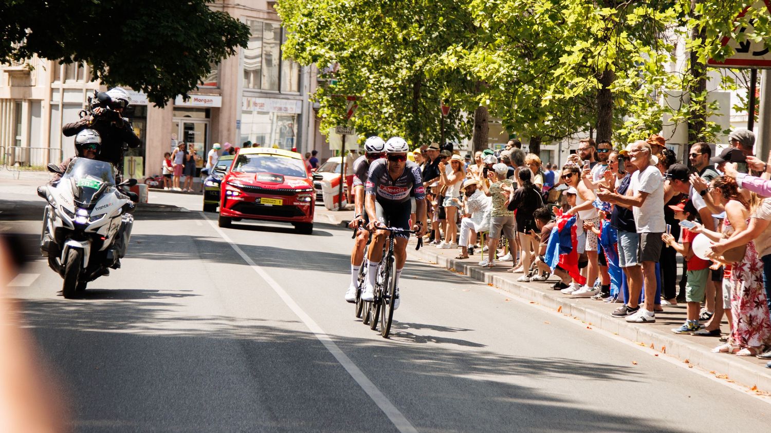 Spectators gather along the edges of a sunny urban street for a public event.