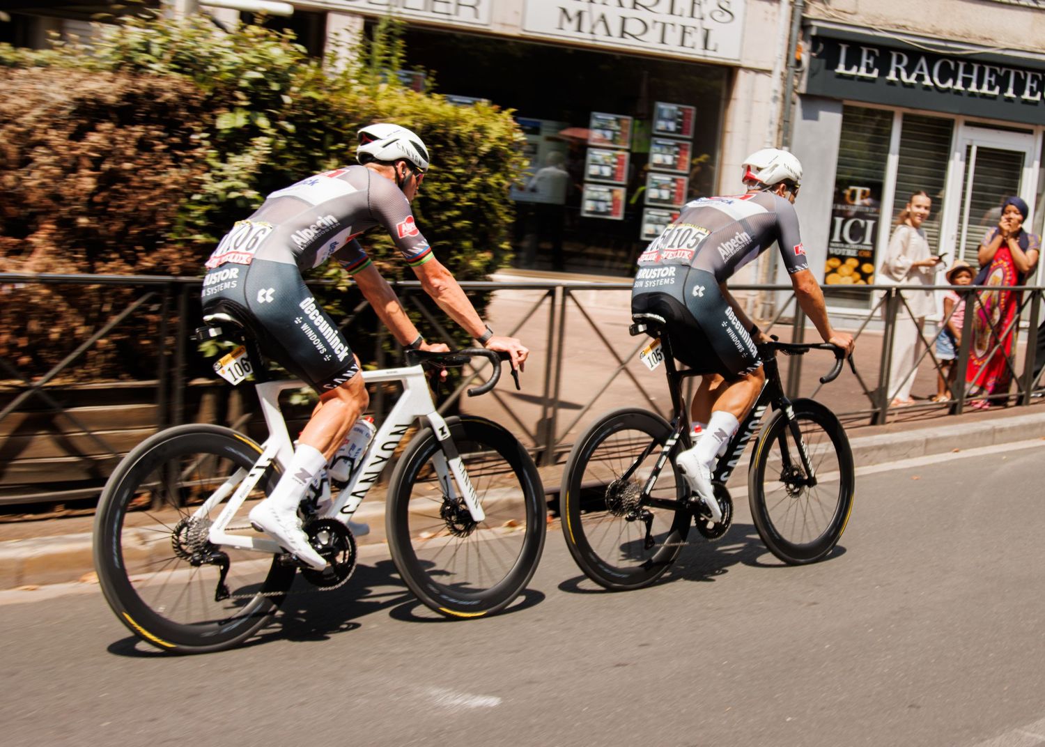Two cyclists racing on professional bikes through a city street.