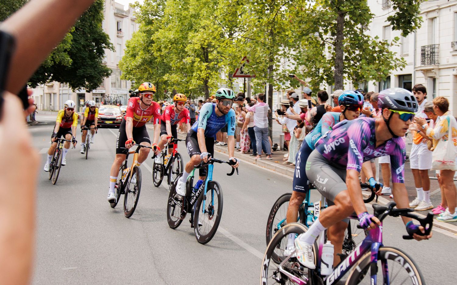 Cyclists compete in a professional road race as spectators line the urban course route.