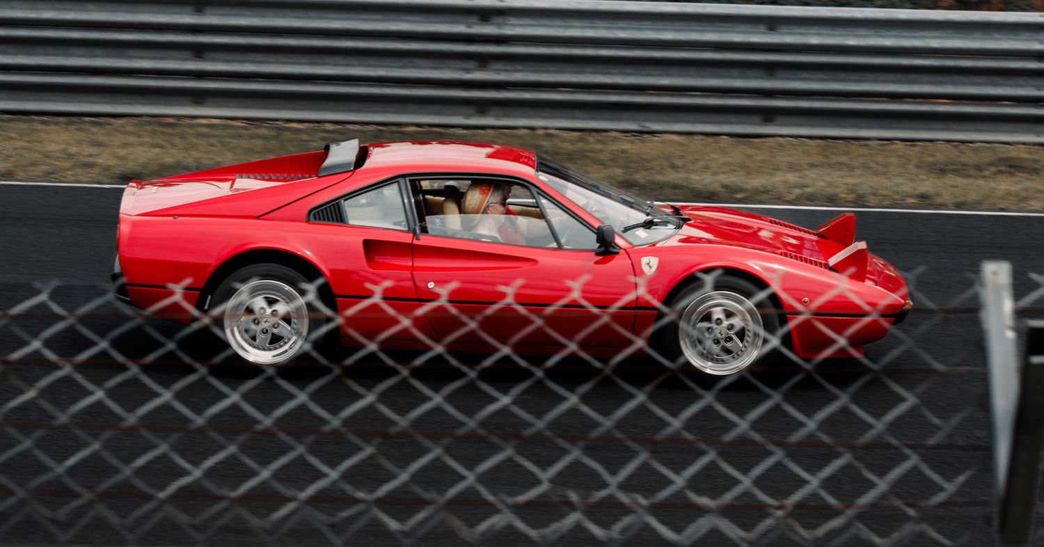 Red Ferrari sports car in motion on race track behind safety fence.