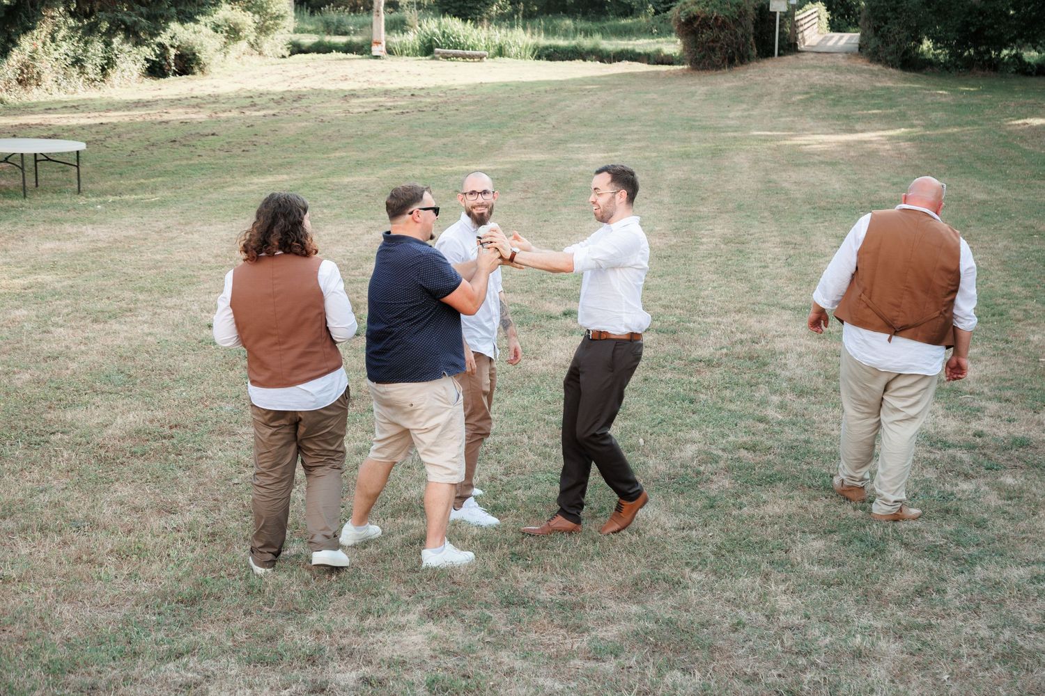 Group of wedding guests in casual attire socializing and playing games on a green lawn.