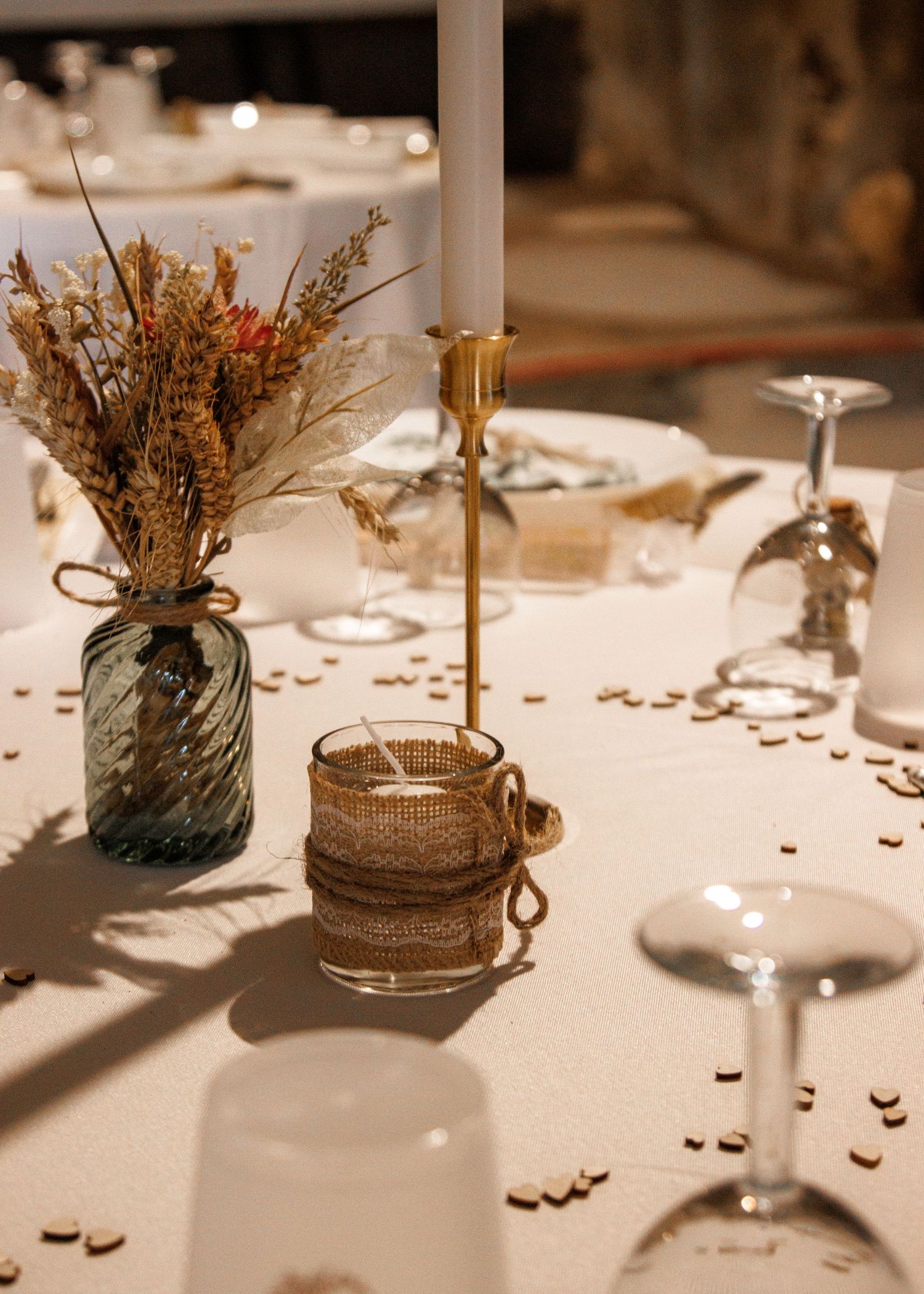 Elegant rustic table decorations feature burlap-wrapped mason jars with dried flowers and white candles at a wedding reception.