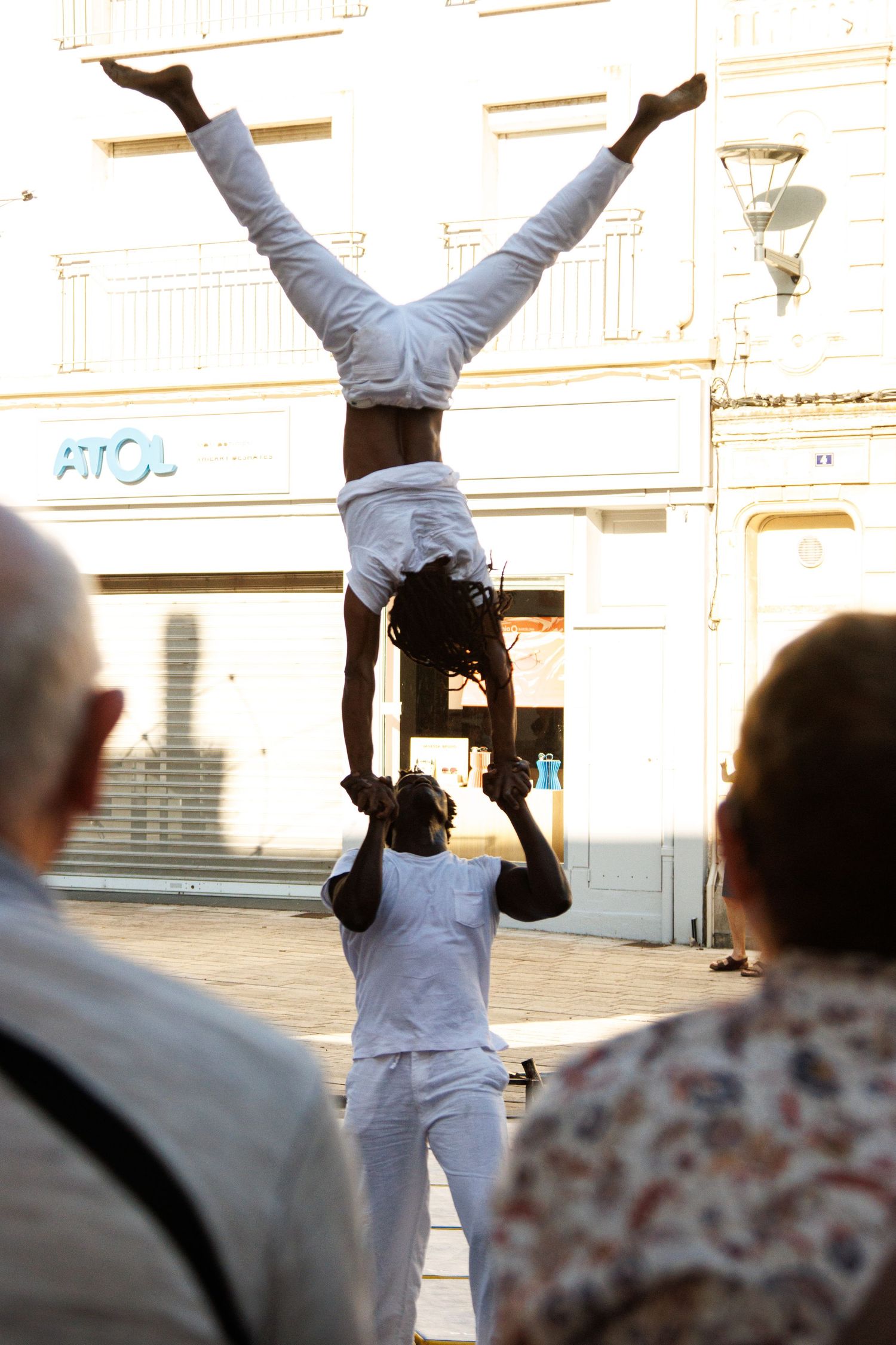 Street performers execute a dramatic inverted handstand balance routine in front of spectators.