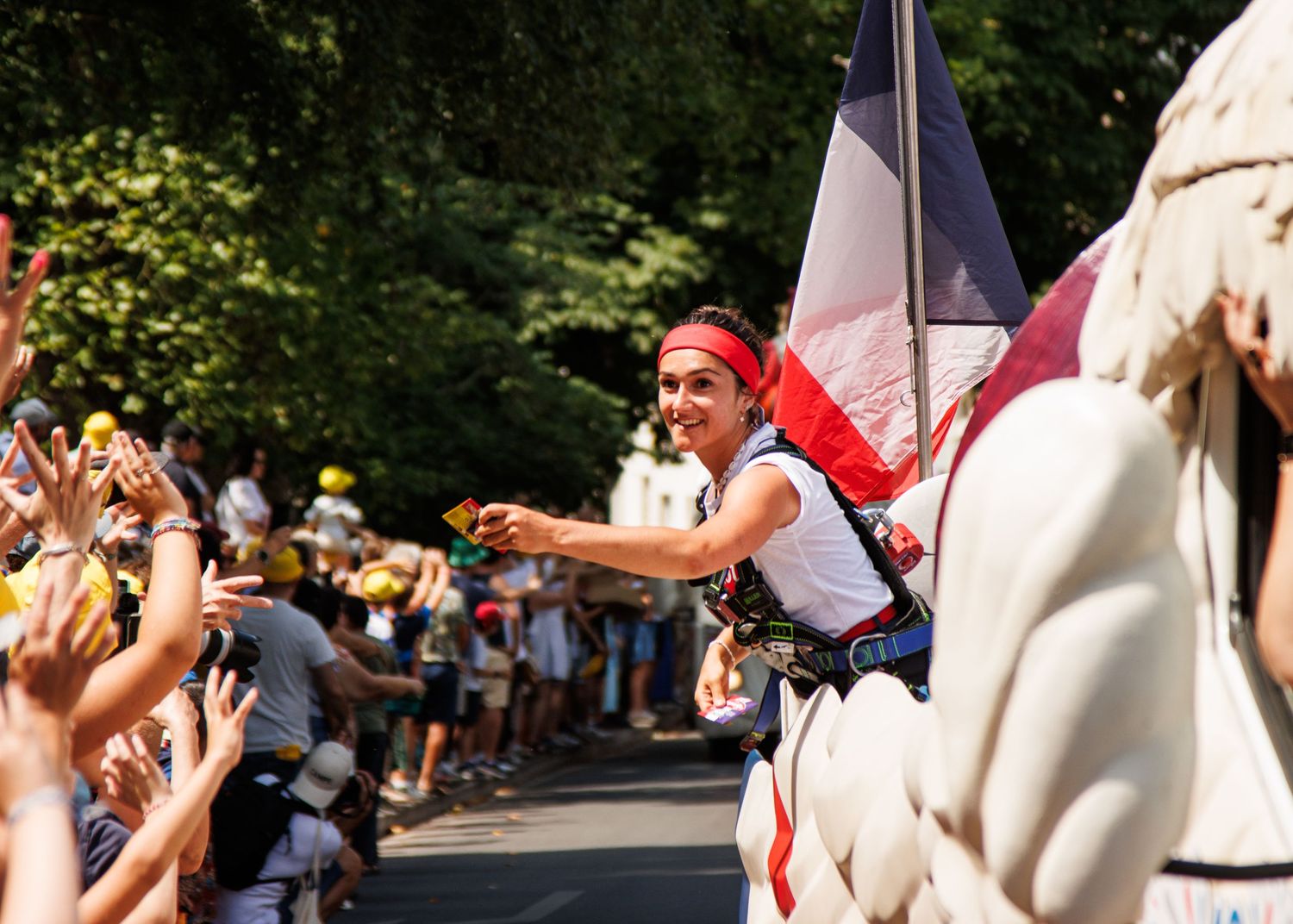 Energetic crowd cheers during a summer parade as performers interact with spectators along a tree-lined street.