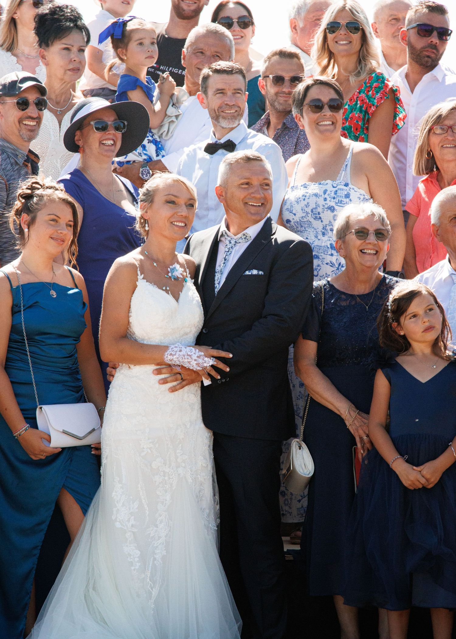 Wedding party and guests pose together for a sunny outdoor group photo.