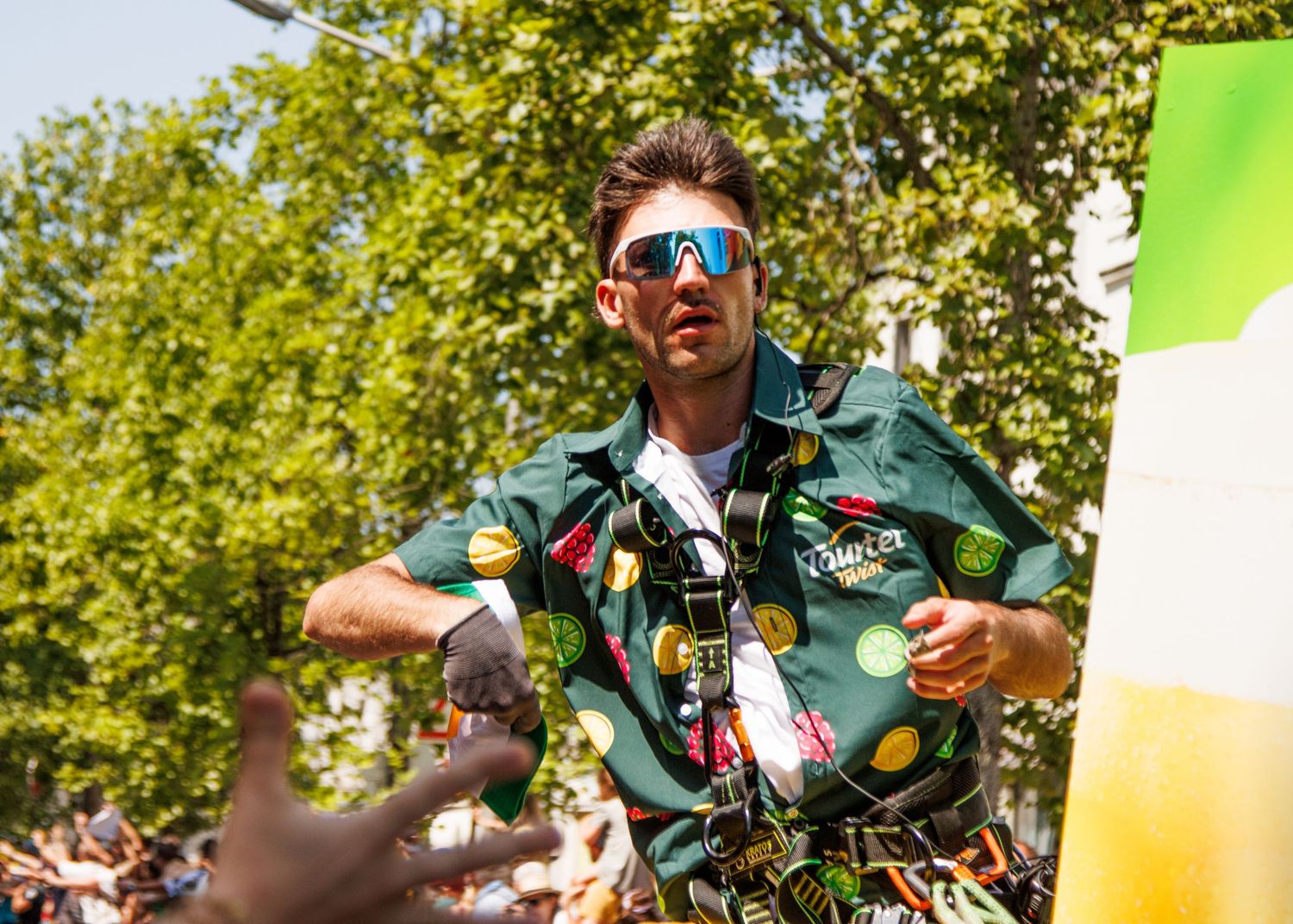 A promotional team member dances on a branded vehicle during a cycling event parade.