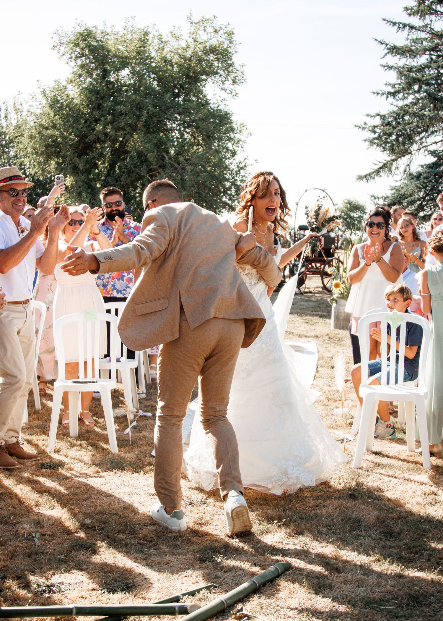 Wedding party dances in a line on sunny outdoor patio wearing neutral colors and enjoying celebration.