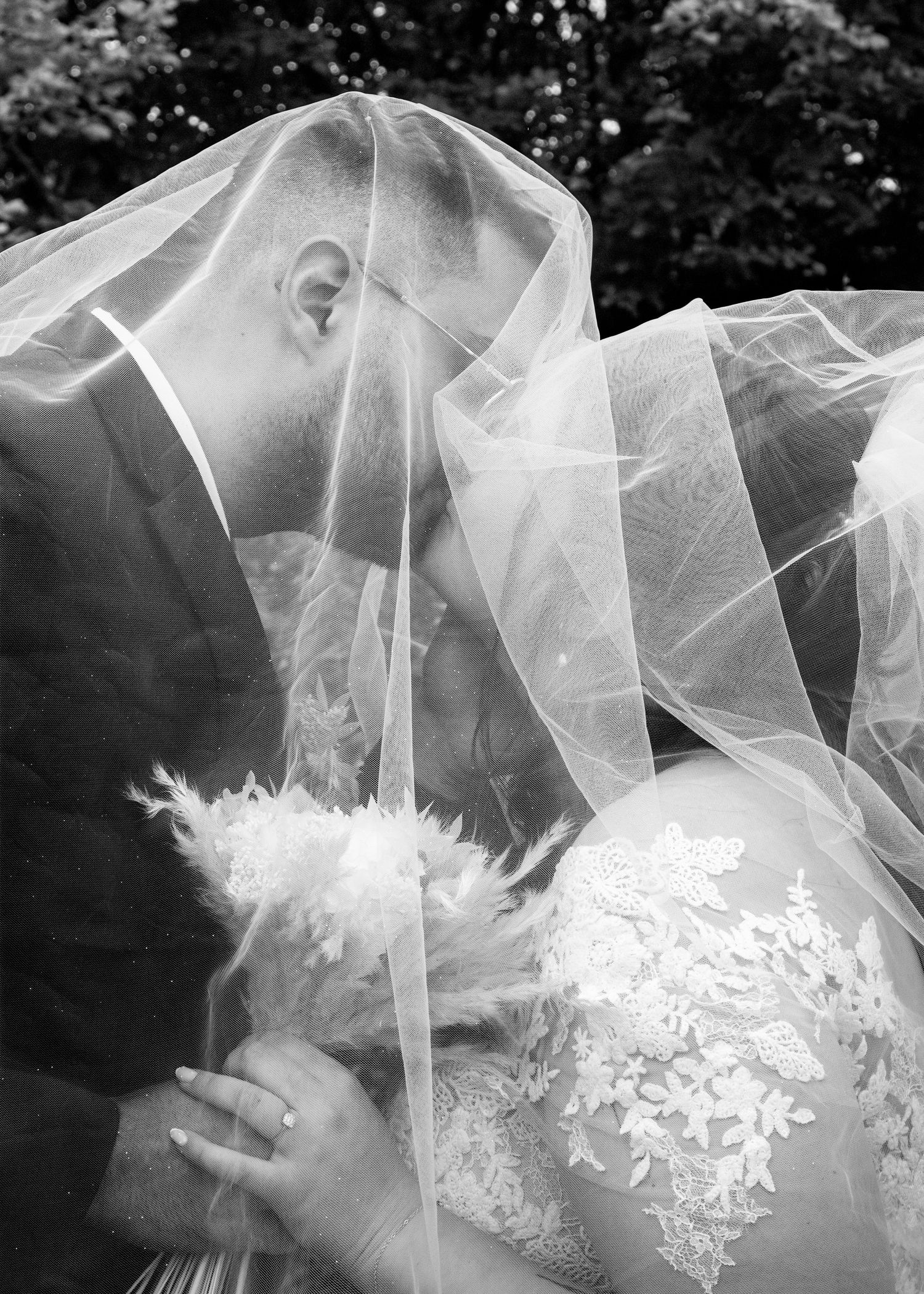 Black and white photo of bride and groom sharing a kiss under a flowing wedding veil.