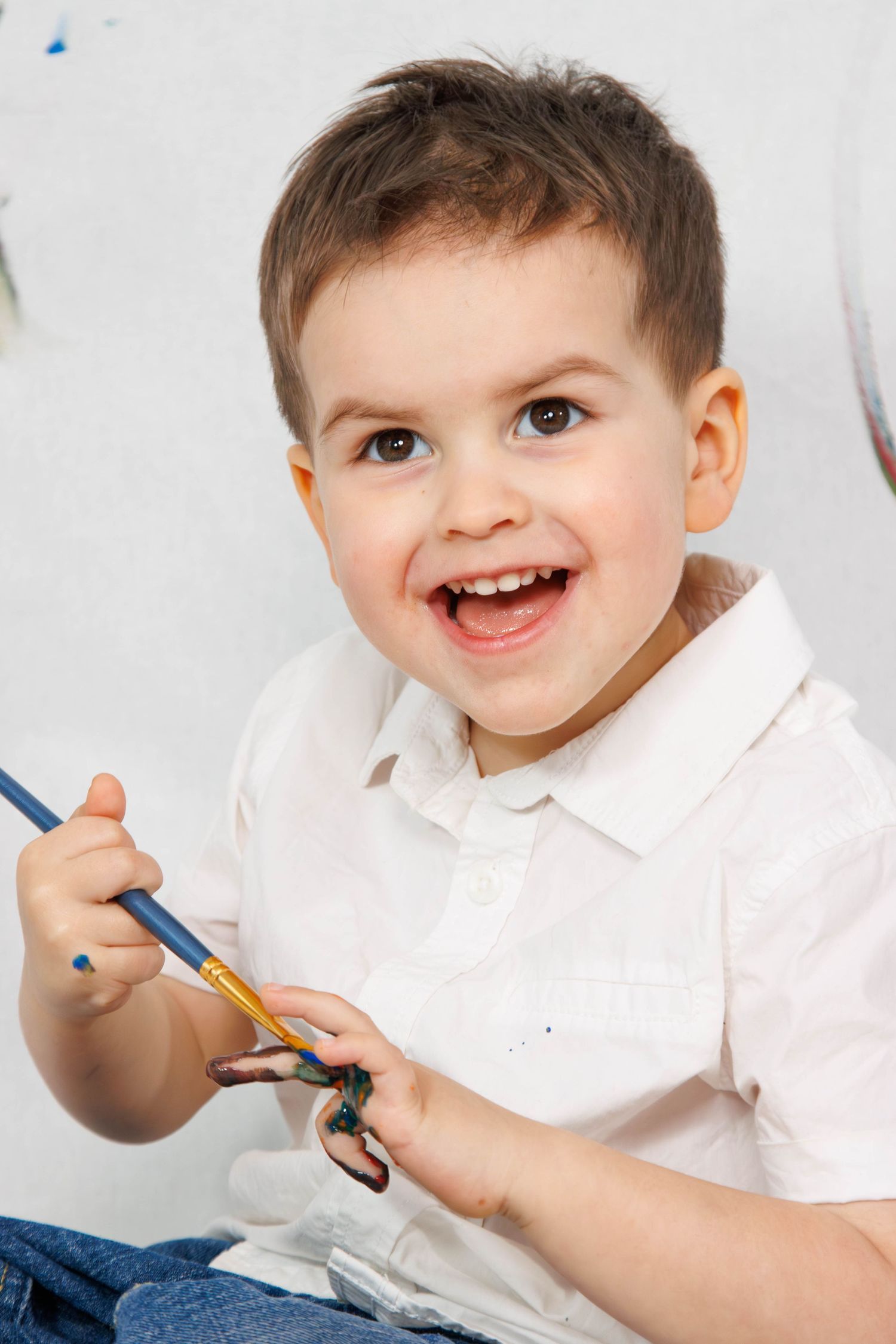 Child in white polo shirt holding blue paintbrush during art activity.