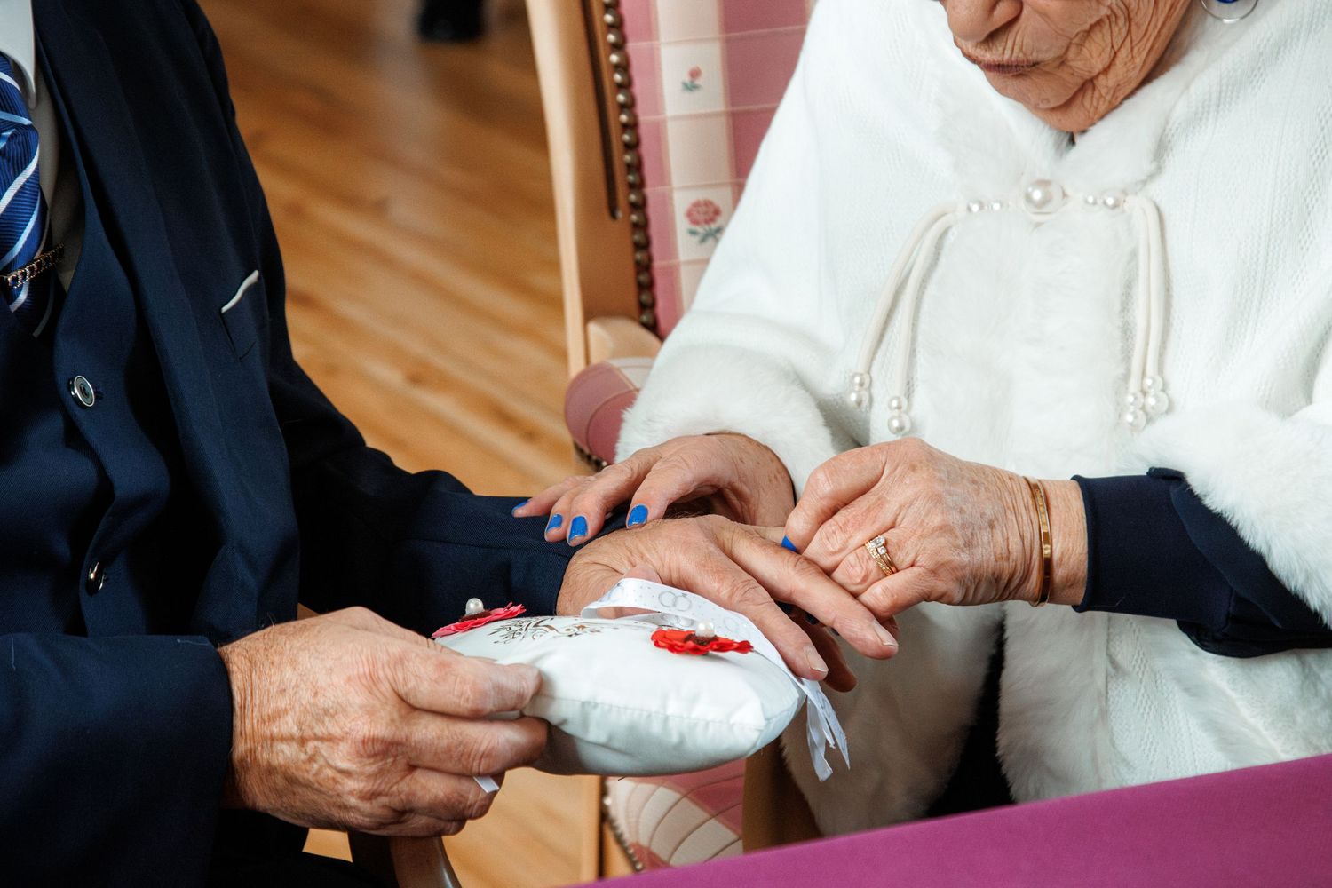 Elderly couple exchanging wedding rings on a white pillow during a marriage ceremony.