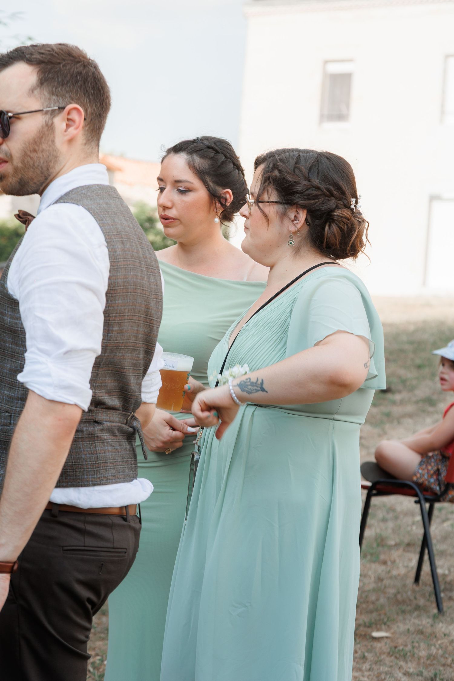 Bridesmaids in mint green dresses socializing with a male guest at an outdoor wedding.