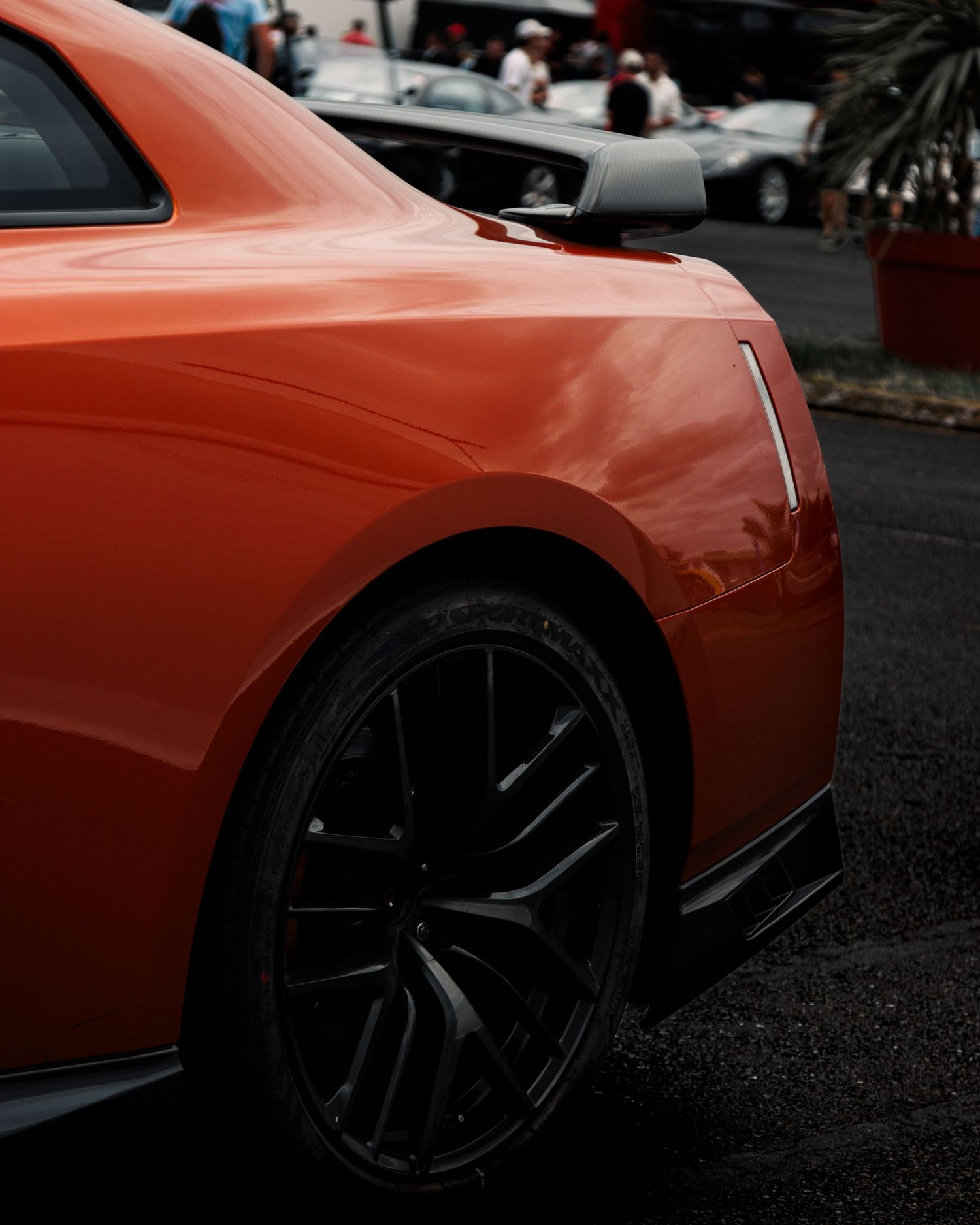 Side profile view of an orange sports car with black alloy wheels parked on asphalt.
