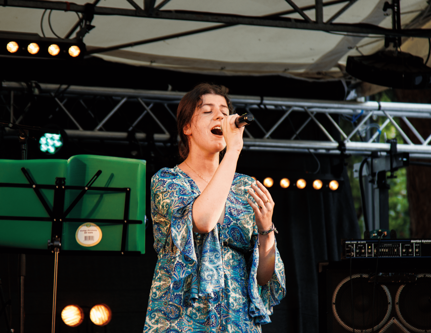 A singer performs passionately on stage wearing a blue patterned dress.