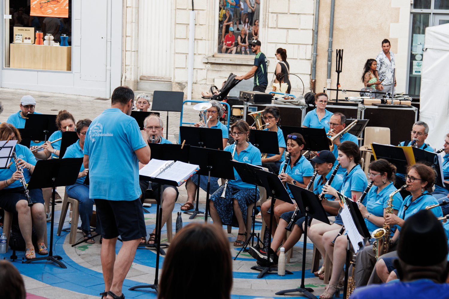 A youth concert band performs in matching light blue t-shirts while being conducted outdoors.