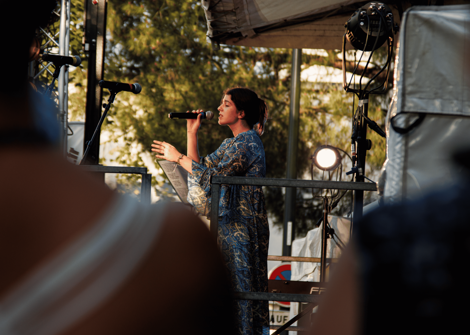 A performer sings on an outdoor festival stage during a sunny afternoon performance.