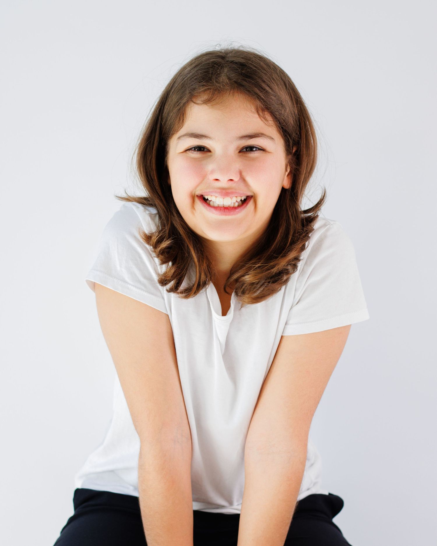 Cheerful person in white t-shirt and dark pants sits on white background in three casual poses.