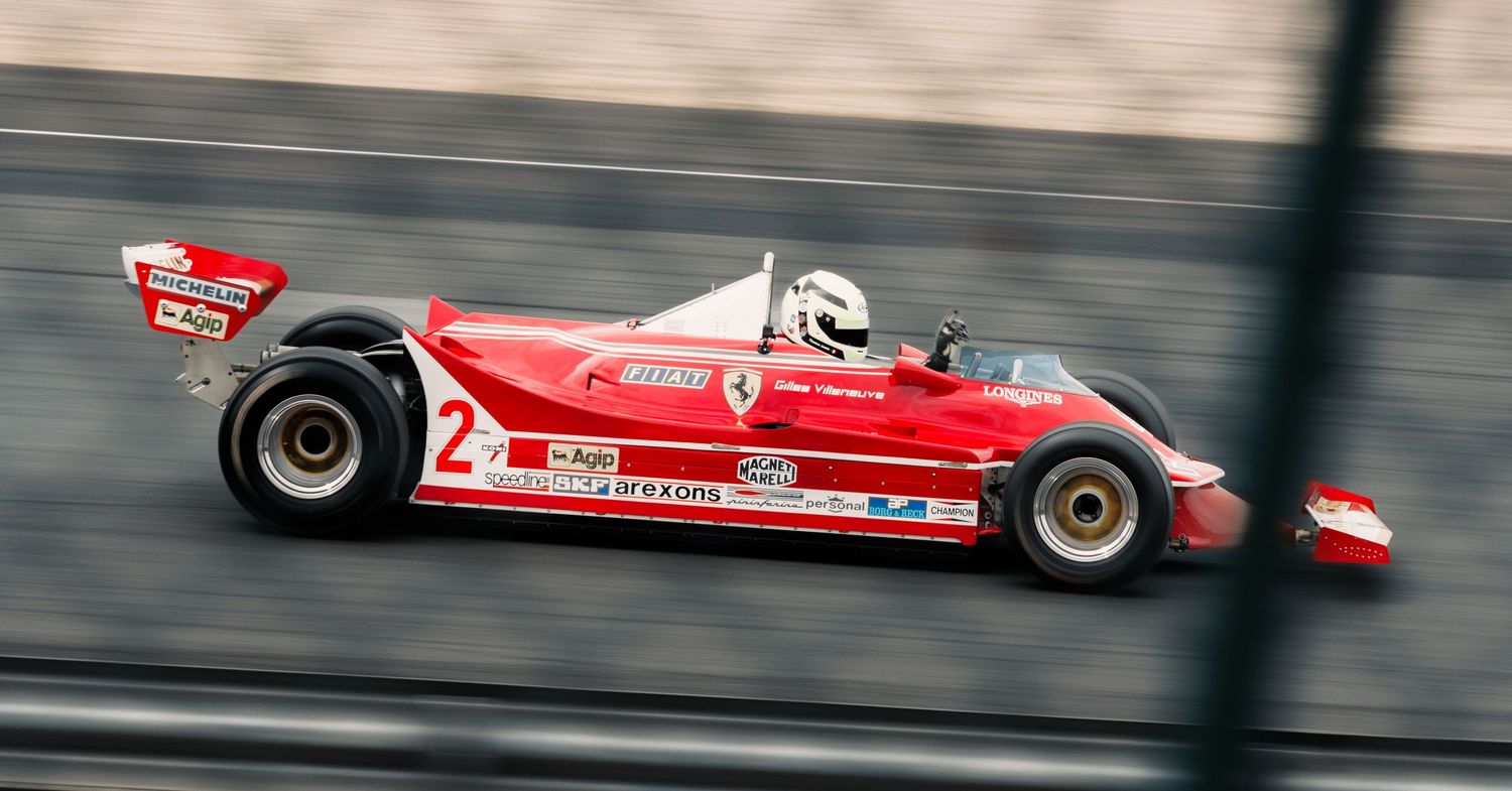Vintage red Formula 1 race car with number 2 speeding past in motion blur on a racetrack.