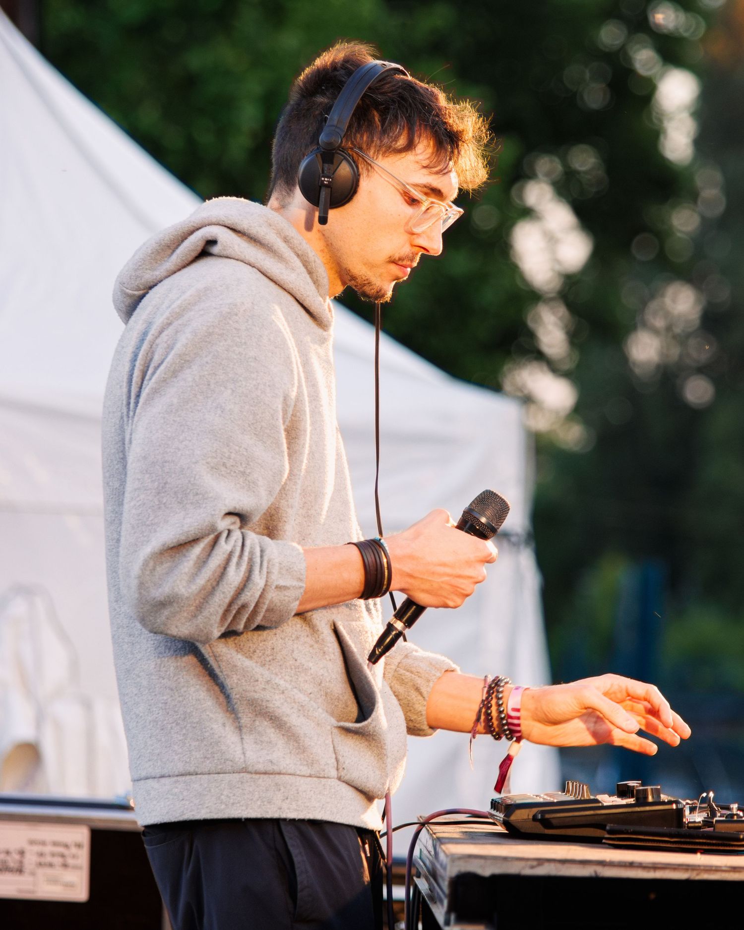 DJ in grey hoodie using equipment at outdoor event.