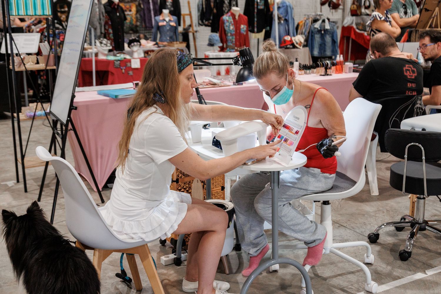 A nail technician wearing a mask performs a manicure on a client at an indoor beauty fair.