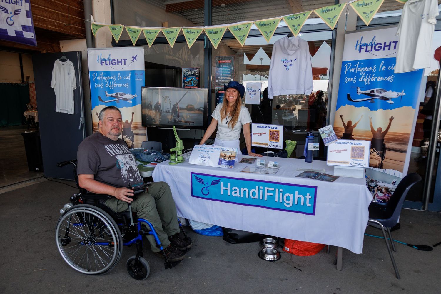 HandiFlight booth at an airshow with a person in a wheelchair and staff member at a table with aviation brochures.