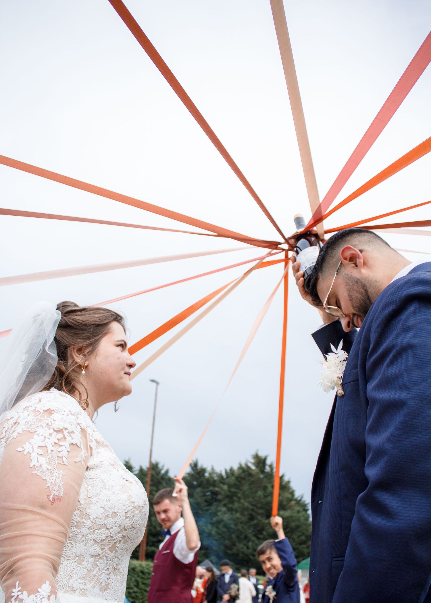Bride and groom stand face to face beneath colorful ribbons at an outdoor wedding ceremony.