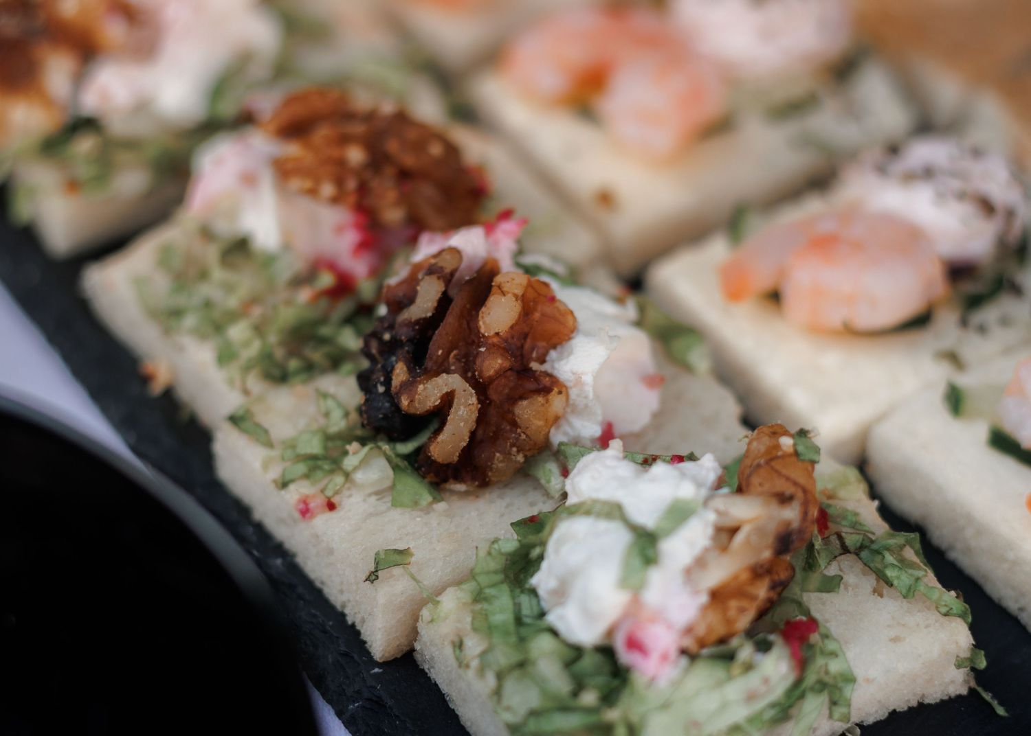 Elegant wedding appetizers on slate board topped with shrimp, walnuts, and cream cheese garnish.