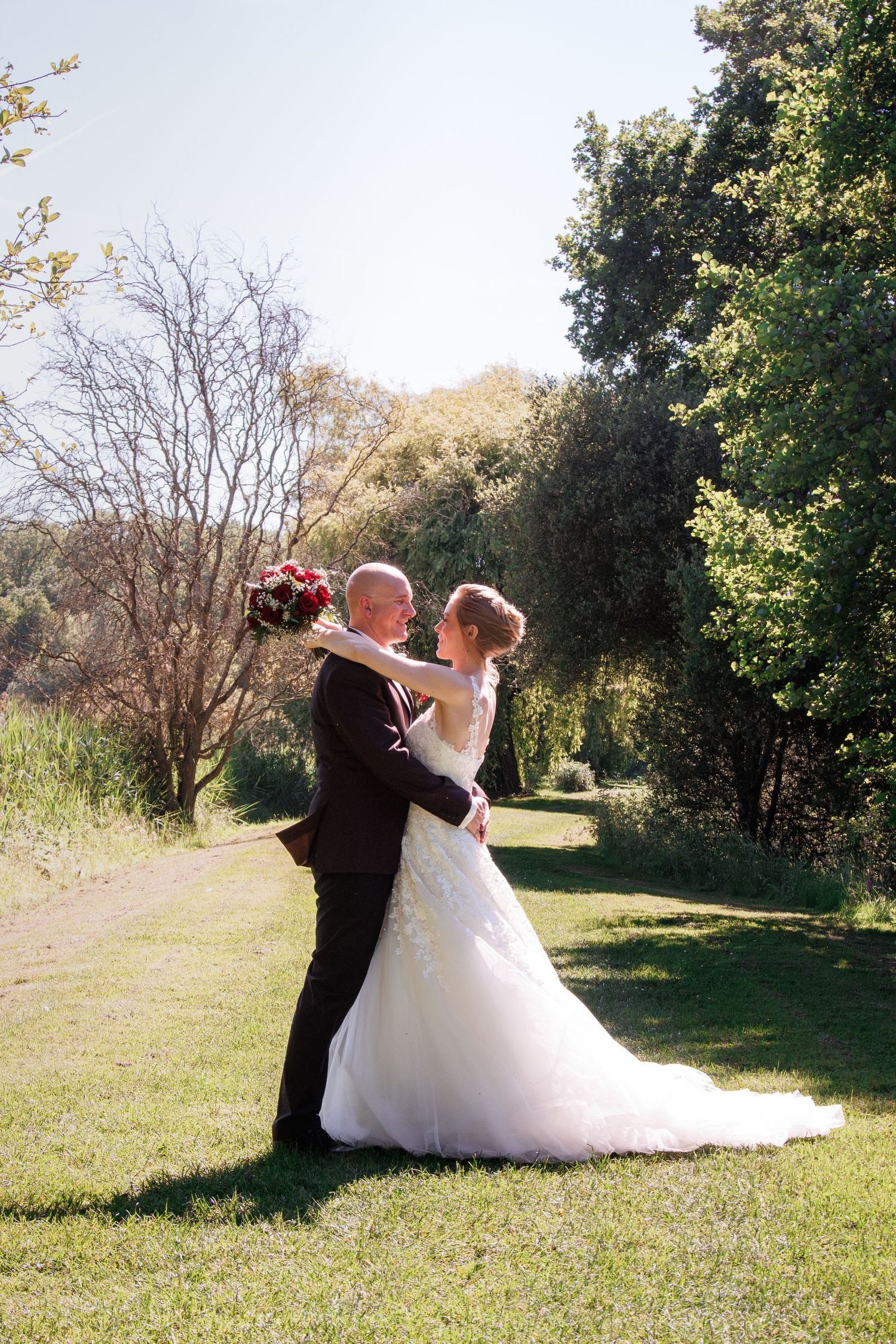 Bride and groom embracing romantically in lush garden on bright sunny wedding day.