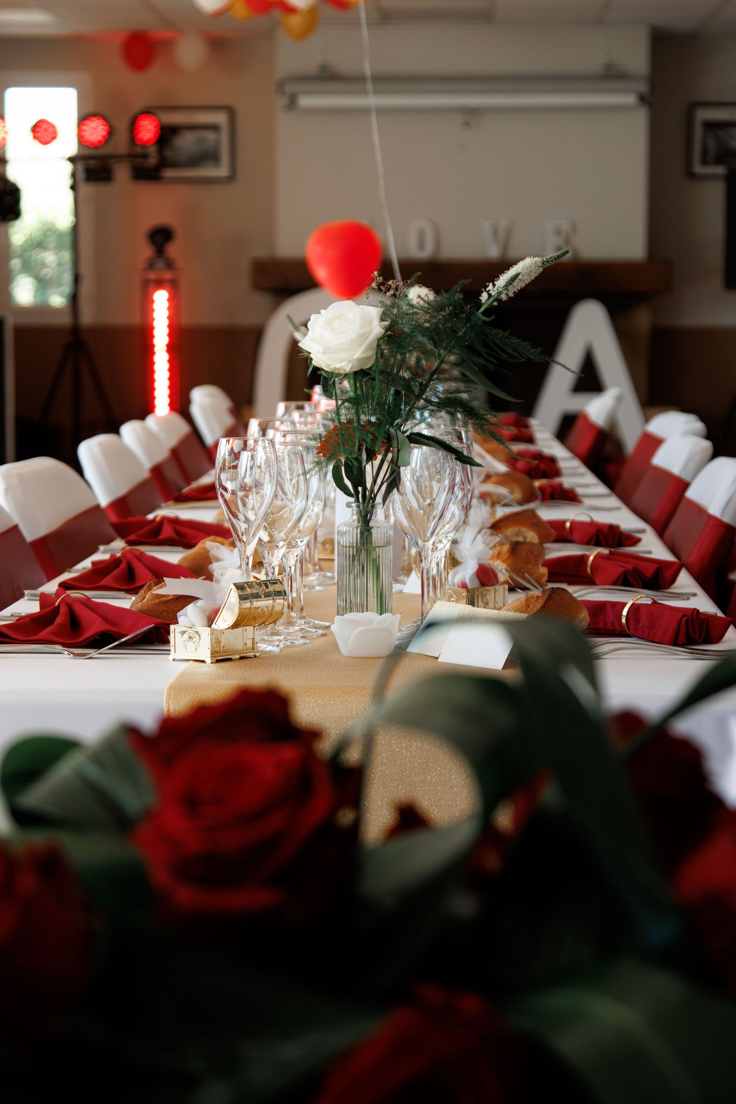 Elegant wedding reception table set with red napkins, crystal glasses, red roses, and white floral centerpiece.
