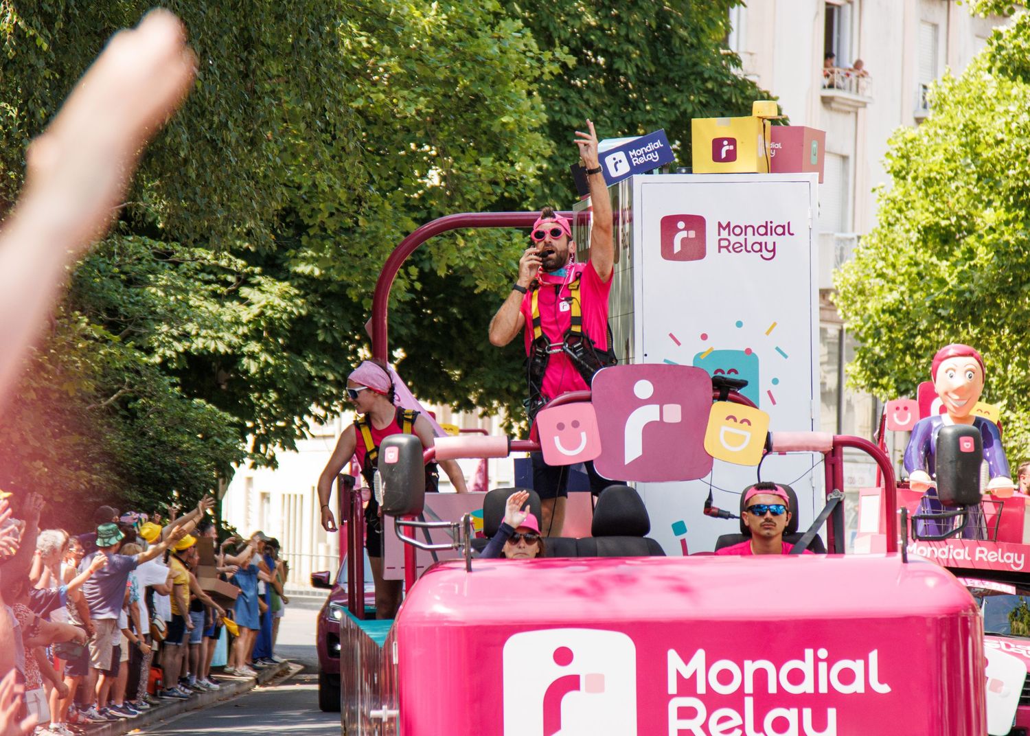 Pink Mondial Paint promotional vehicle drives through a parade route as crowds watch from the sides.