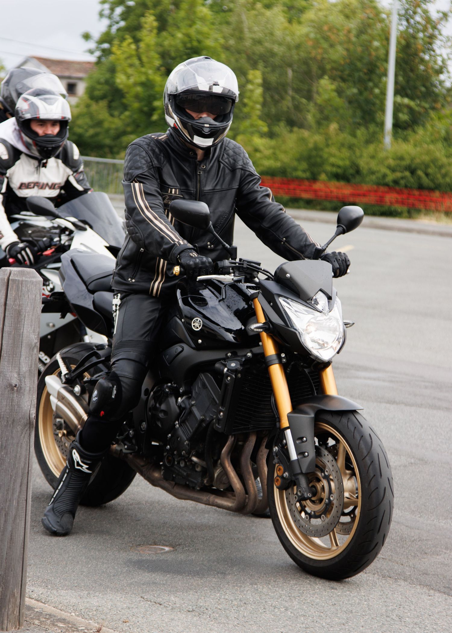 Motorcyclist in black protective gear riding sleek black sport bike on paved road.