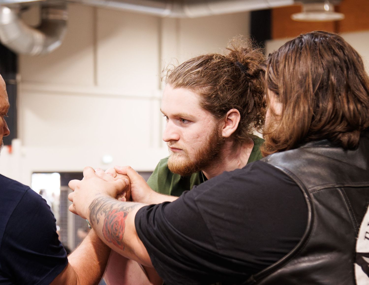 Intense arm wrestling competition underway as competitors grip hands while others watch.