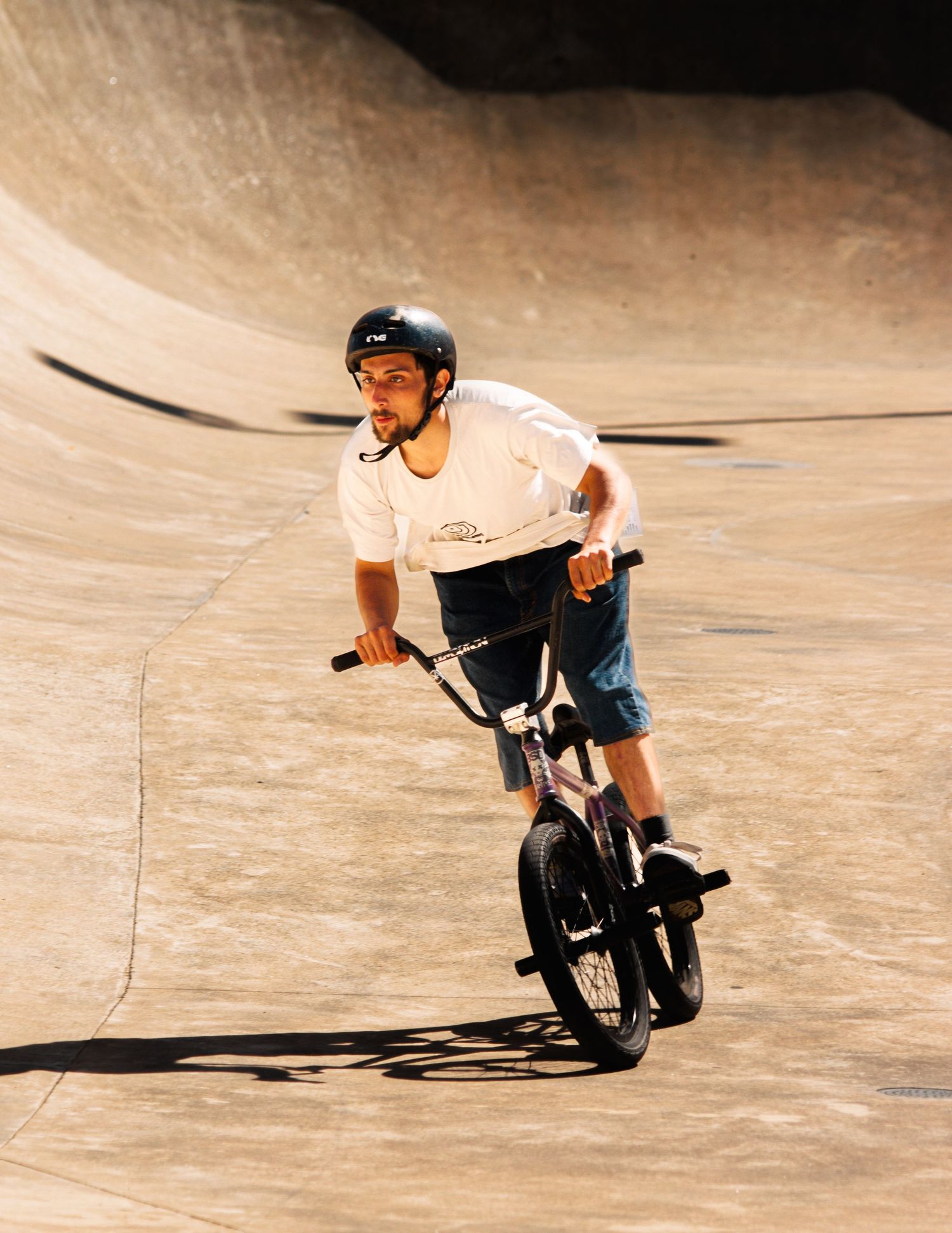 BMX rider performing tricks on a curved wooden ramp in an indoor skate park.