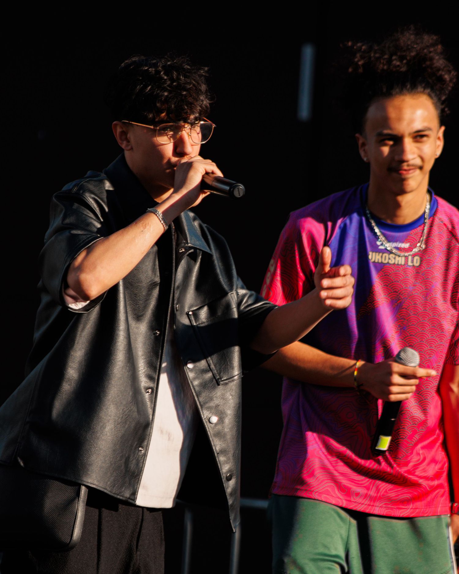 Musicians performing on stage with one wearing bright pink t-shirt and black leather vest.