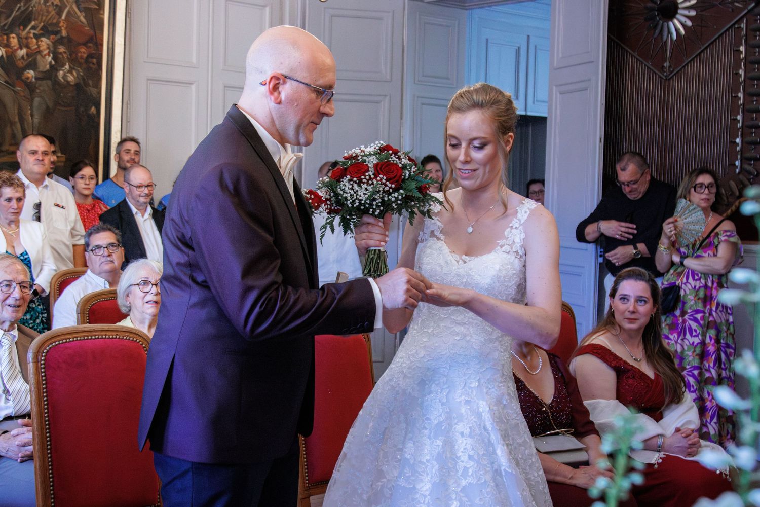 A groom places a ring on his brides finger during a wedding ceremony with guests seated.