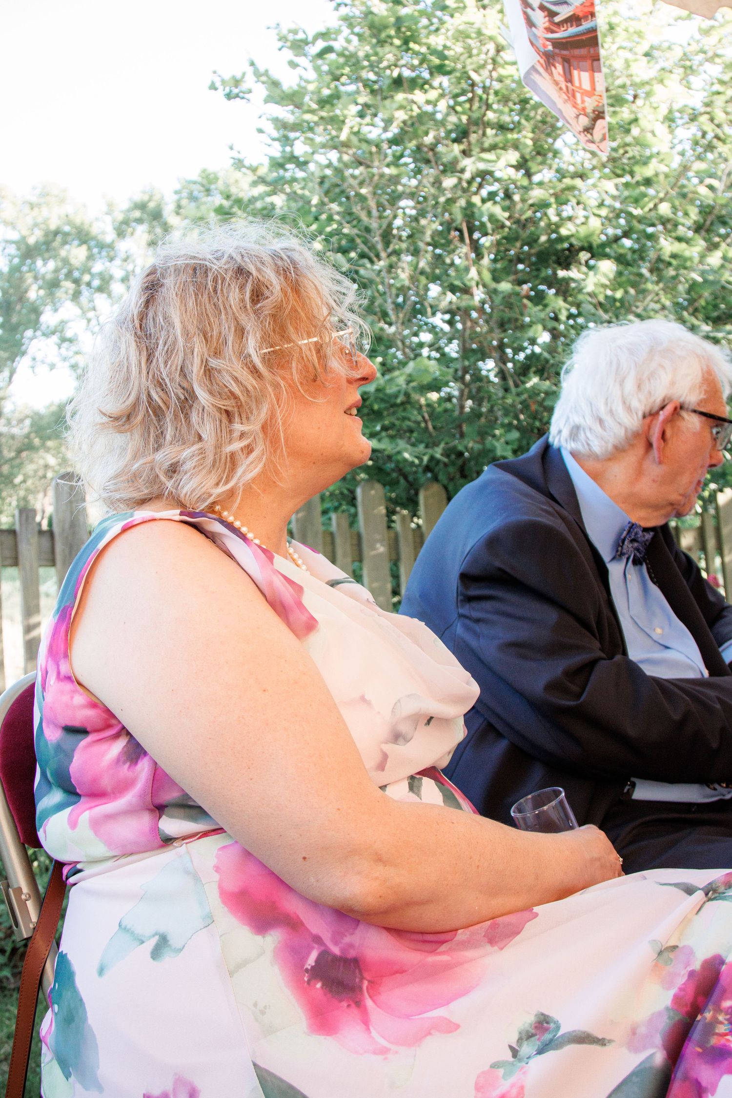 Senior couple sitting together outdoors at a wedding reception in garden setting.