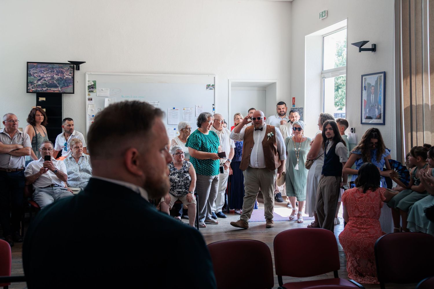 Guests standing and socializing in a bright reception hall during a formal event or wedding ceremony.