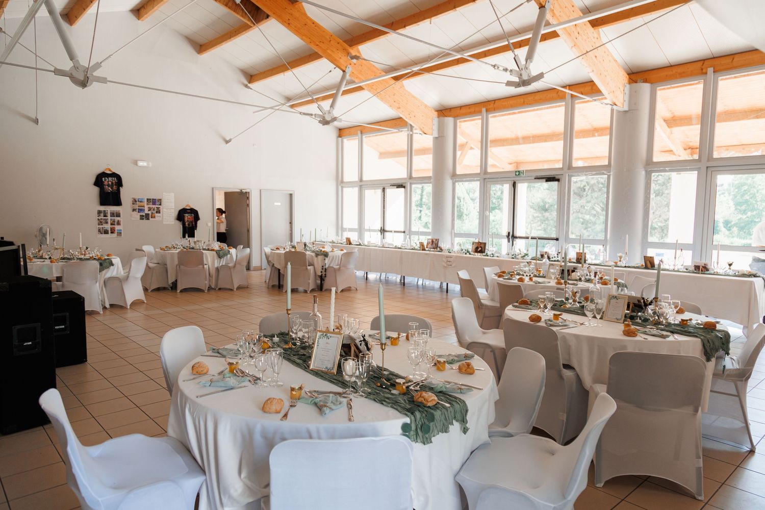 Elegant wedding reception hall with round tables, white chairs, and wooden beam ceiling.