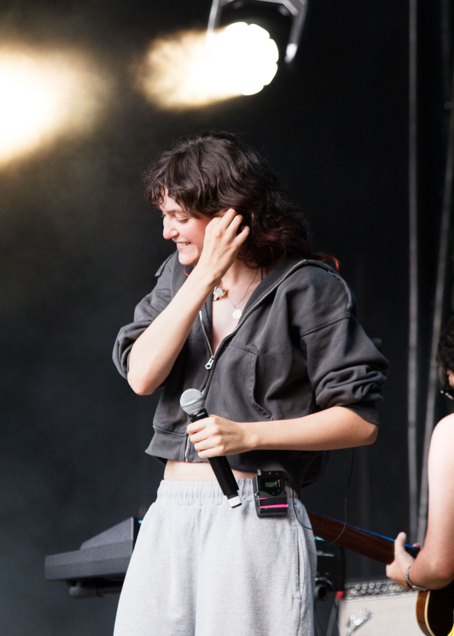 Young woman performing on stage holding a microphone, wearing a gray cropped hoodie and light sweatpants.