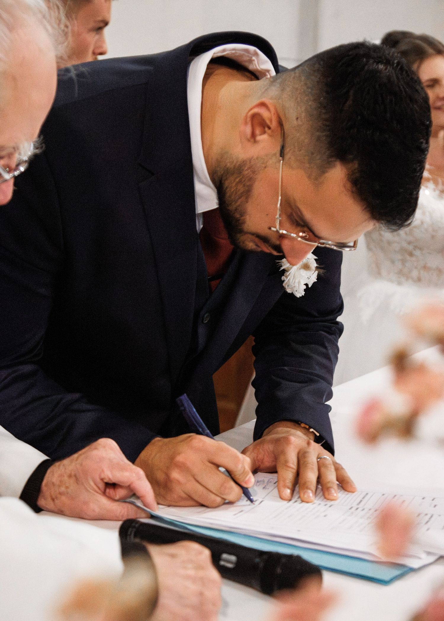 Man in navy suit signing wedding register document with pen at ceremony table.