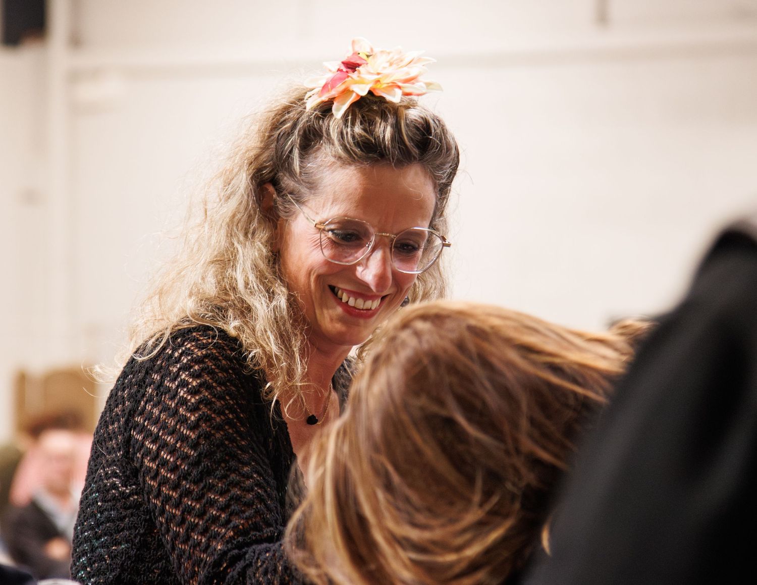 Person with curly hair and glasses laughing during indoor gathering.