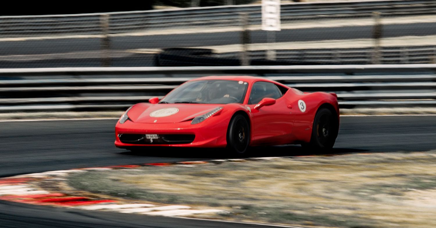 Red Ferrari 458 Italia races through a technical section of racetrack.