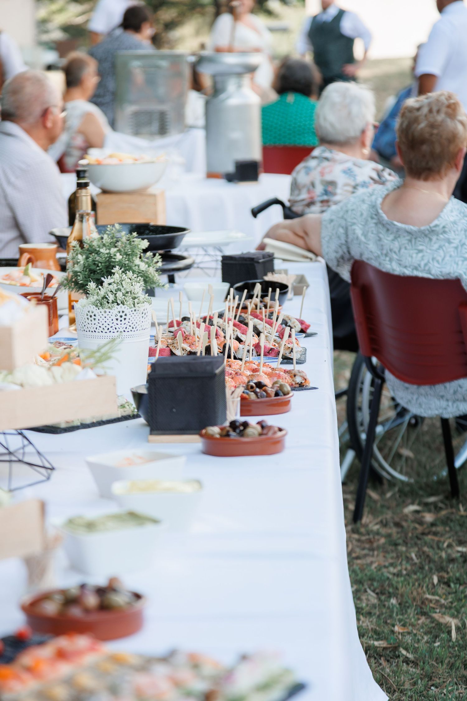 Elegant outdoor wedding reception buffet table with skewered appetizers and guests seated behind.