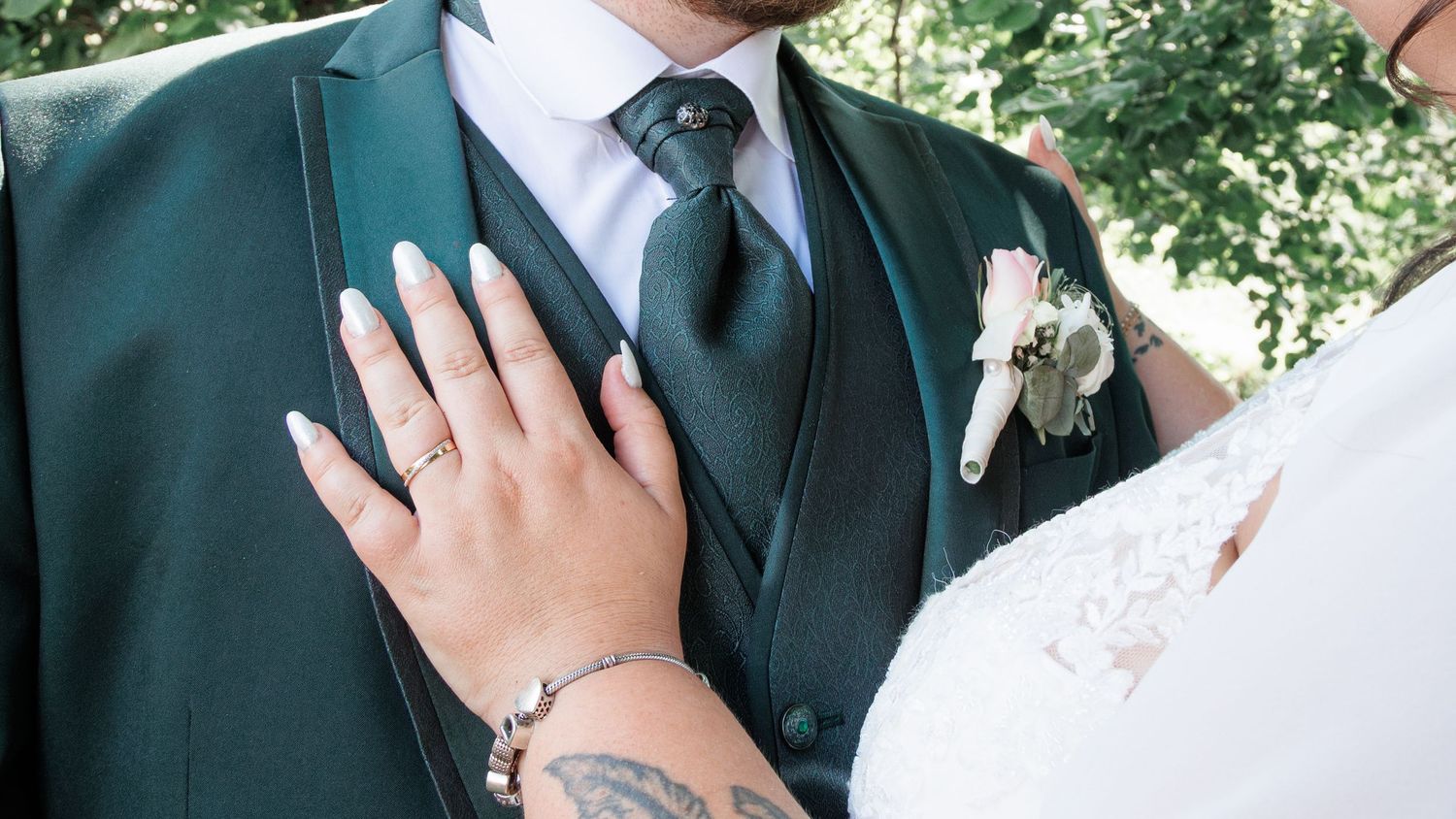 Close-up of bride's hand with manicured nails resting on groom's dark green wedding suit.