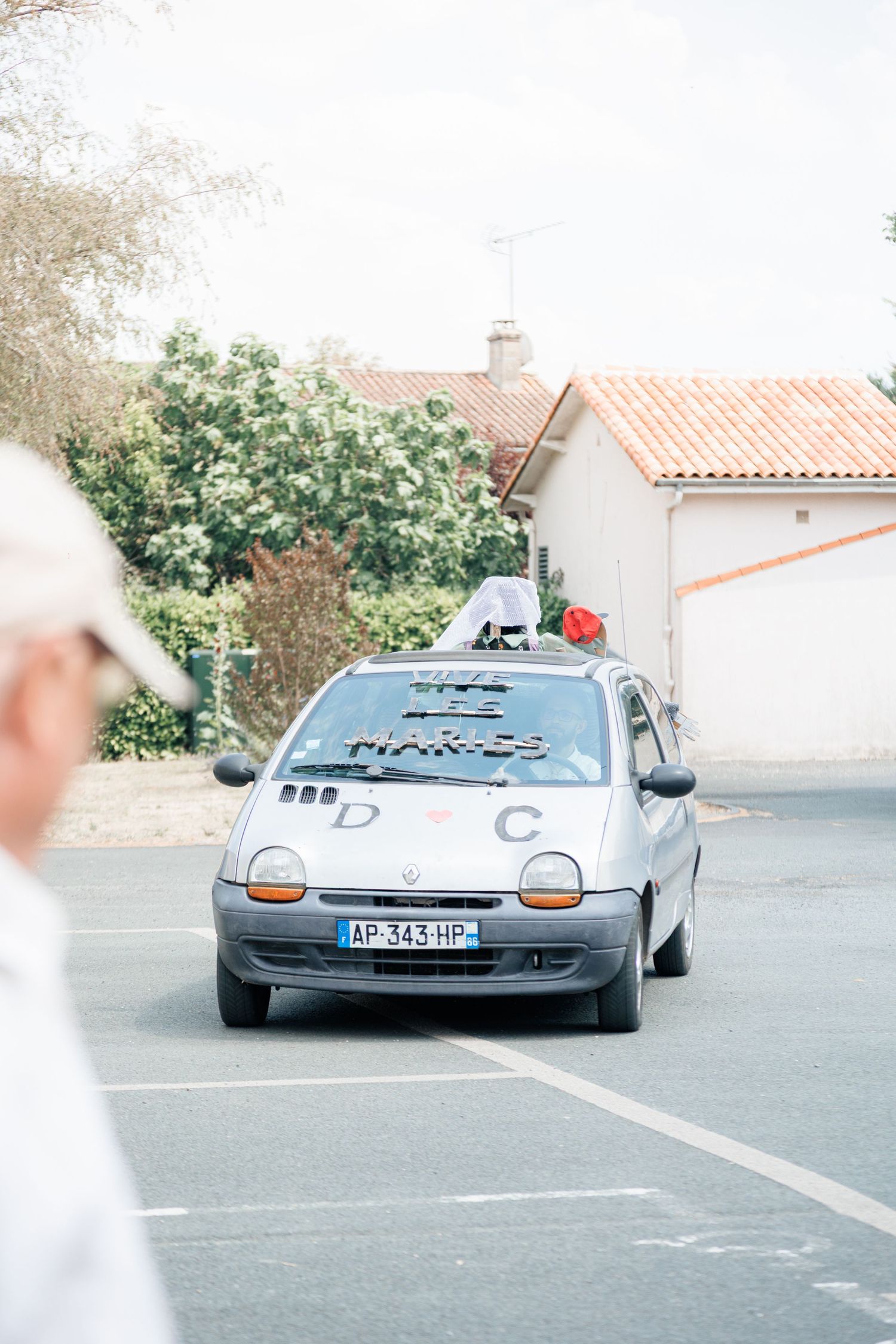 Silver Renault Twingo wedding car with decorations driving through a French village street.