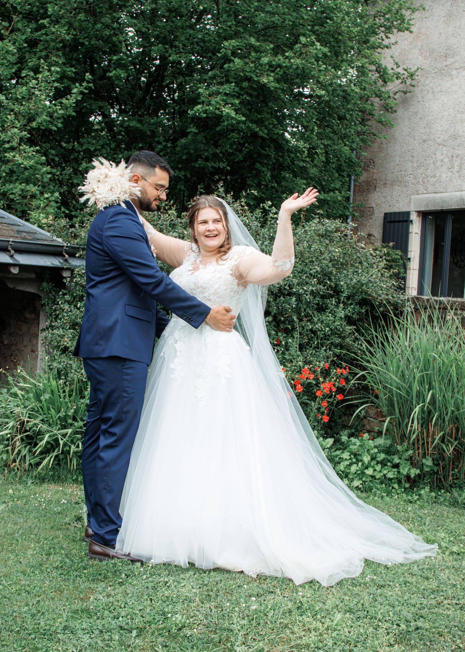 Bride in white tulle gown and groom in navy suit share a joyful dance outdoors on their wedding day.