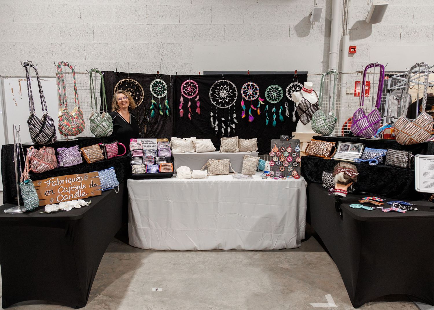 Vendor booth displaying colorful handbags, dreamcatchers, and decorative pillows at an indoor craft fair.