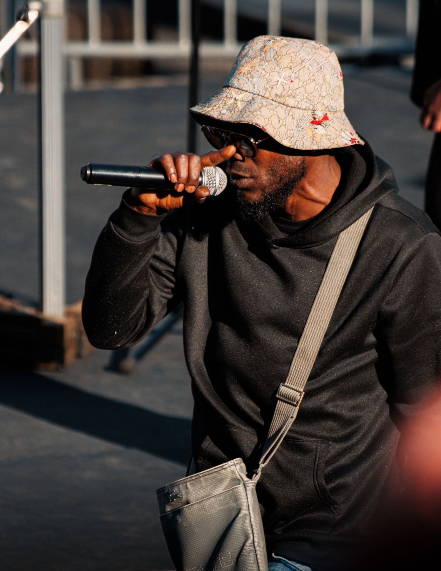 Performer in bucket hat and black hoodie singing into microphone.