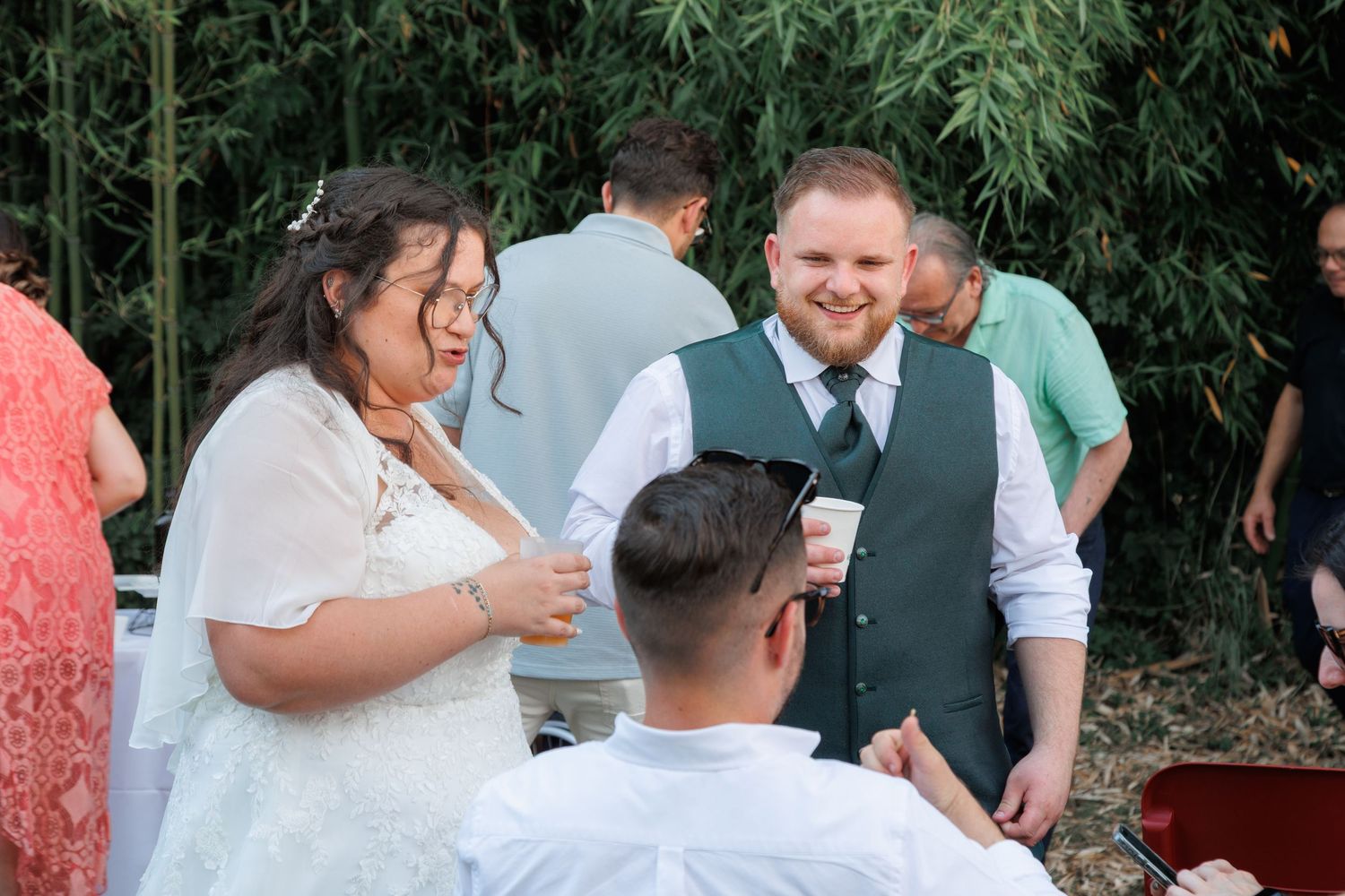 Bride and groom smiling and chatting with guests during outdoor wedding cocktail hour in garden setting.